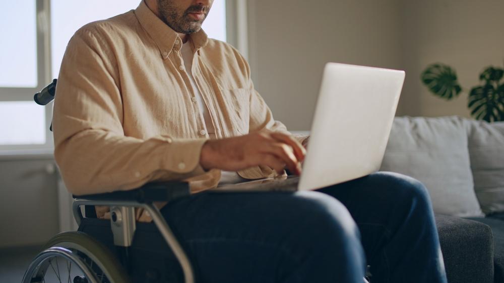 A man in a wheelchair is focused on using a laptop, engaged in work or communication.