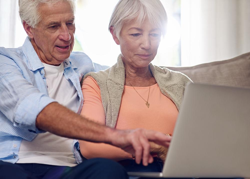 An older couple sitting together, focused on using a laptop computer at a cozy home setting.