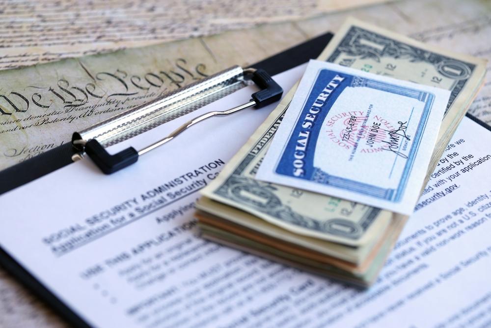 A Social Security card and cash rest on a clipboard holding a Social Security benefits application.